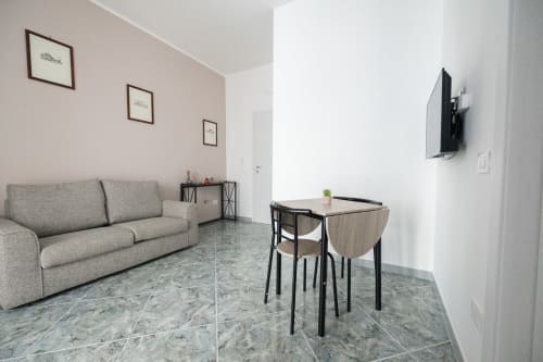 Soggiorno moderno dell'appartamento Newhouse Modugno con divano grigio, tavolo da pranzo, TV a parete e pavimentazione in marmo