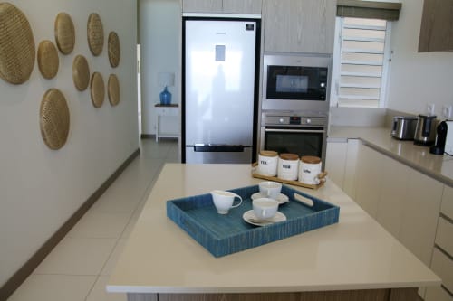 Modern kitchen in Pointe d'Esny luxury apartment with white counters, blue tray, coffee station, and decorative woven wall