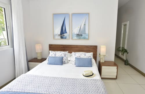 Bright beachfront bedroom at Unik Properties with sailing artwork, wood headboard, blue accents, and sea views