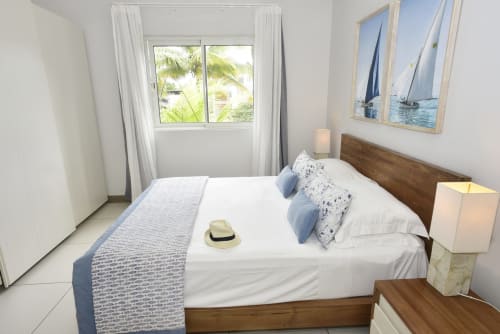 Bright beachfront apartment bedroom in Pointe d'Esny with sea view, wooden bed, white linens, and palm tree views through
