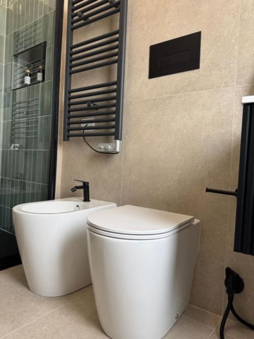 Bagno moderno in Maison ì Room con bidet e WC bianchi, scaldasalviette nero, piastrelle beige e accessori neri