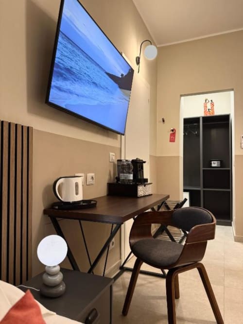 Moderno spazio di lavoro in camera d'hotel con TV, scrivania, sedia in legno, bollitore e macchina del caffè presso Maison ì Room a Reggio Calabria