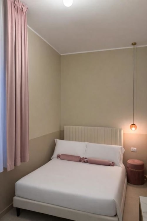 Accogliente camera matrimoniale a Maison ì con tende rosa, biancheria bianca, lampada a sospensione e vista sul giardino a Reggio Calabria