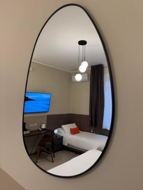 Riflesso dello specchio della camera da letto che mostra il letto con cuscino rosso, scrivania, TV a schermo piatto, luci a sospensione e tende con vista sul giardino