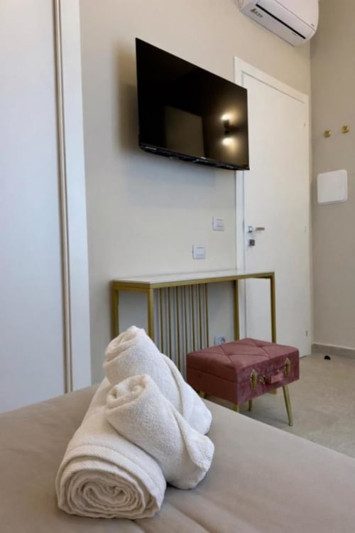 Camera moderna a Maison ì con asciugamani arrotolati, TV a parete, pouf bordeaux e unità di climatizzazione a Reggio