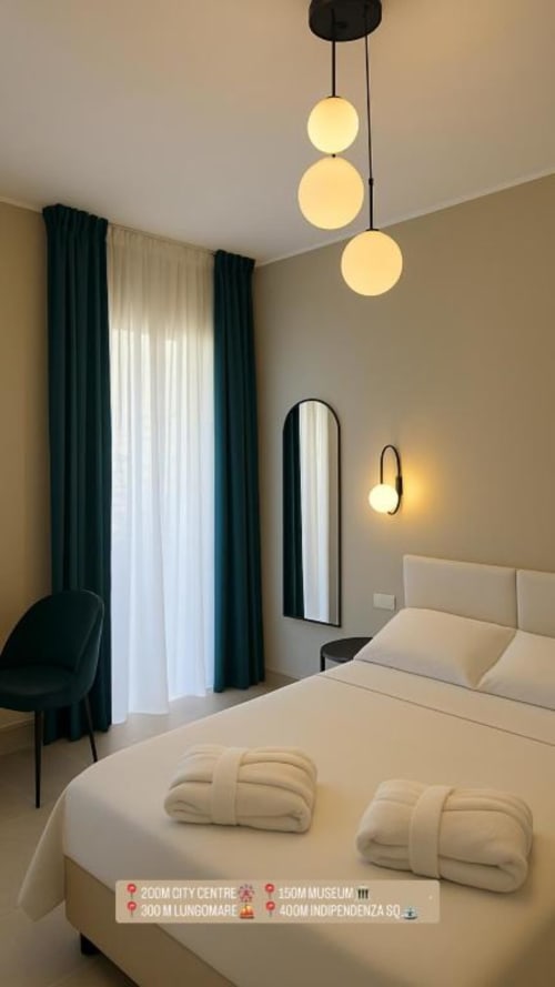 Camera moderna a Maison ì a Reggio Calabria con lampade a sospensione, biancheria color crema, tende blu petrolio e arredamento contemporaneo