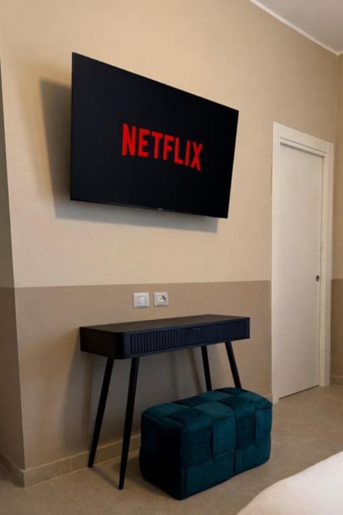 Netflix in streaming su TV a schermo piatto nella camera dell'hotel Maison ì Room a Reggio Calabria, con scrivania e sedute blu