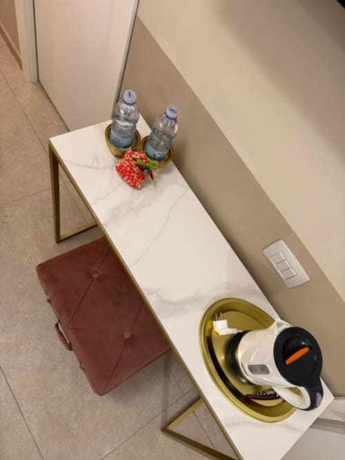 Scrivania della camera d'hotel presso Maison ì con due bottiglie d'acqua, fragola fresca, cuffie in una ciotola dorata e sedia color borgogna.