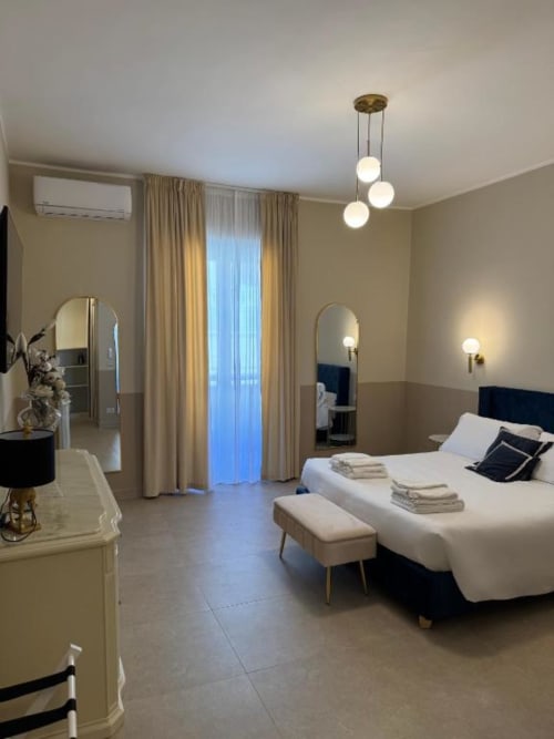 Elegante camera matrimoniale deluxe presso Maison ì a Reggio Calabria con letto bianco, specchi, lampade a sospensione, accesso al balcone e vista mare
