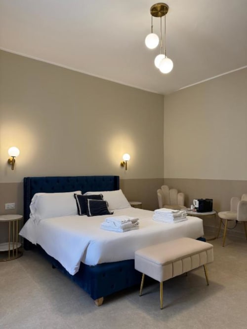 Camera doppia di lusso presso Maison ì a Reggio Calabria con letto imbottito blu scuro, biancheria bianca, lampade a sospensione in ottone e design moderno