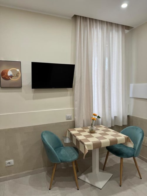 Suite moderna a Maison ì Room a Reggio Calabria con tavolo da pranzo, sedie turchesi, TV a parete e tende trasparenti