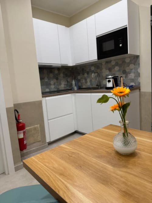 Cucina moderna in appartamento a Reggio Calabria con armadiature bianche, rivestimento grigio, tavolo in legno e fiori gialli in vaso
