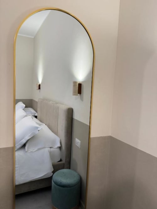 Specchio ad arco con cornice dorata che riflette una camera moderna con biancheria bianca nell'appartamento di Reggio Calabria