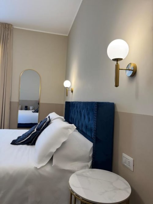 Camera moderna di Maison ì Room con testata imbottita blu scuro, applique in ottone e arredamento elegante a Reggio Calabria