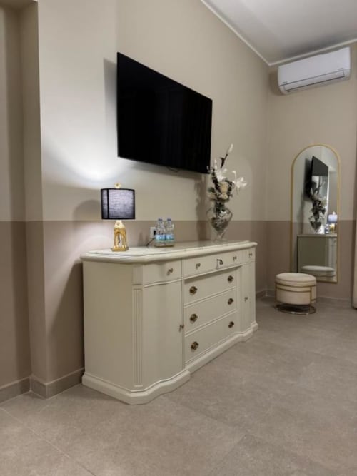 Camera elegante presso Maison ì Room a Reggio Calabria con comò color crema, TV a parete, specchio e arredamento moderno