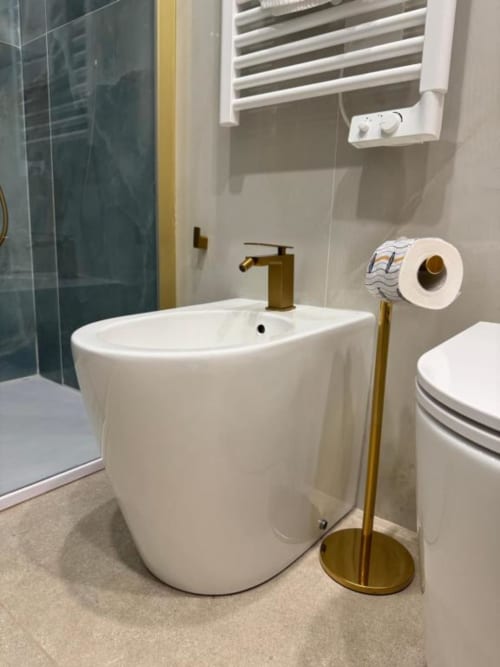 Bagno moderno con lavabo bianco su piedistallo, rubinetto in ottone, bidet e portarotolo nella suite deluxe di Maison ì Room a Reggio