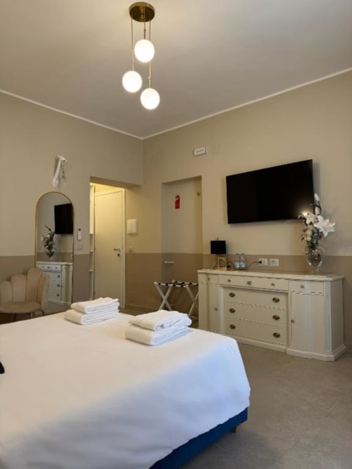 Camera moderna Maison ì con letto matrimoniale, TV a muro, cassettone bianco, lampade a sospensione e pareti beige bicolore