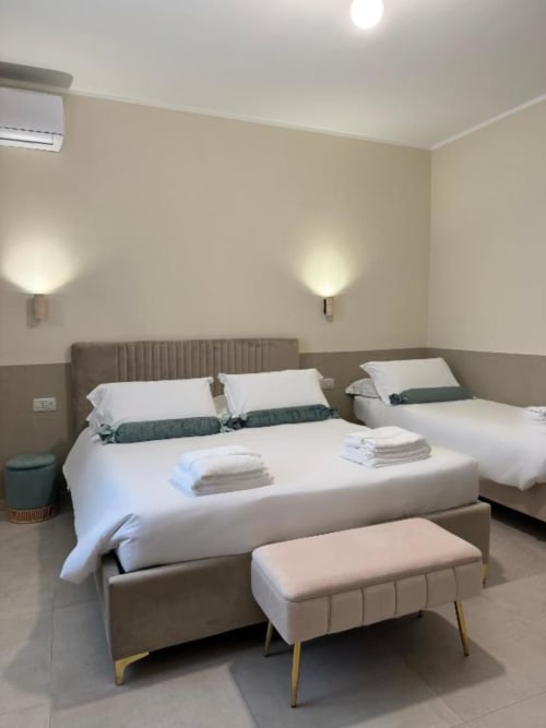Camera moderna a Maison ì Room a Reggio Calabria con letto matrimoniale, letto singolo, dettagli verdi, applique da parete e tonalità beige.