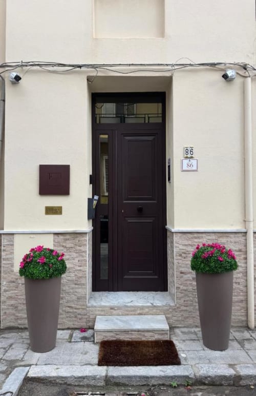 Elegante ingresso della Maison ì Room a Reggio Calabria con porta scura, fiori rosa e facciata moderna