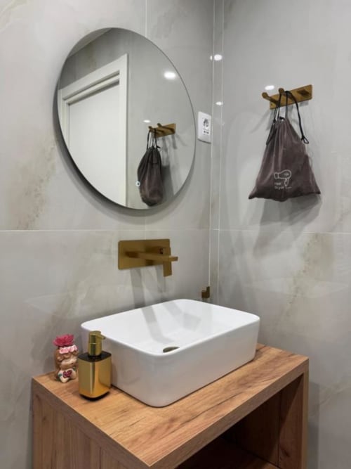 Bagno moderno in Maison ì Room con lavabo bianco, specchio rotondo, mobile in legno, finiture in ottone e appendiabiti neri