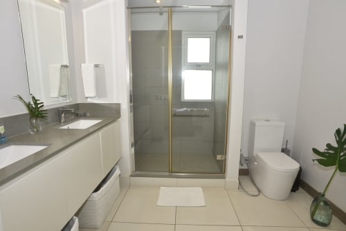Modern bathroom at Pointe d'Esny Summer Luxury Apartment with glass shower, vanity, toilet, and beige tiling.