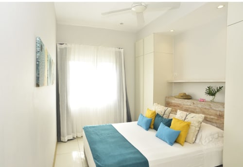 Modern beachfront apartment bedroom in Pointe d'Esny with sea view, colorful pillows, wooden headboard, and natural lighting