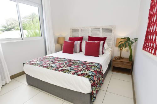 Bright beachfront bedroom with queen bed, red accents, tropical plant, and sea view at Unik Properties Pointe d'Esny