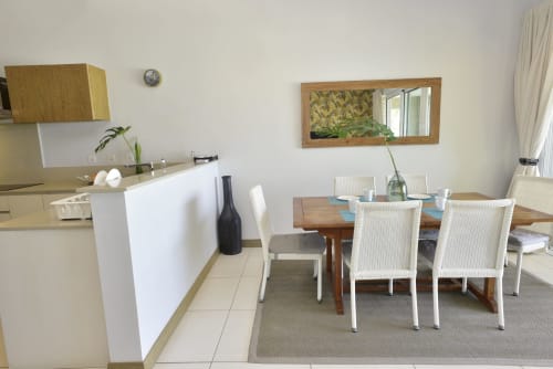 Modern dining and kitchen area in Pointe d'Esny beachfront apartment with wooden table, white chairs, and sea view mirror
