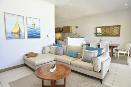 Bright beachfront apartment living room with cream sectional sofa, sailboat artwork, round wooden coffee table, and sea views