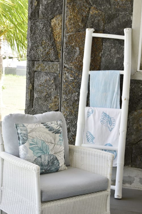 Coastal apartment sitting area with white wicker chair, leaf-patterned pillow, and white towel ladder at Pointe d'Esny