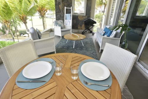 Elegant dining setup at Pointe d'Esny beachfront apartment with round wooden table, blue placemats, and ocean view through