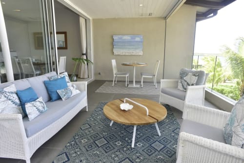 Beachfront luxury apartment terrace at Unik Properties with white wicker furniture, wooden table, and sea views in Pointe