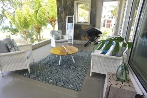 Bright beachfront apartment sitting area with wicker chairs, round wooden table, patterned rug, and sea views through large