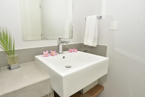 Modern bathroom with white vessel sink, gray tile backsplash, and pink flowers at luxury beachfront apartment in Pointe