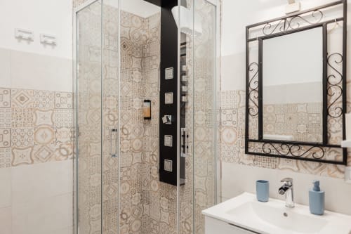 Salle de bain moderne du Casanova B&B Cefalù avec carrelage à motifs, douche vitrée, miroir décoratif et accessoires bleus