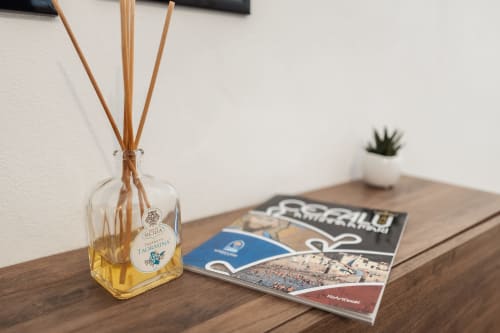 Scrivania in legno nella camera del Casanova B&B con diffusore di midollino, riviste di viaggio e pianta grassa a Cefalù
