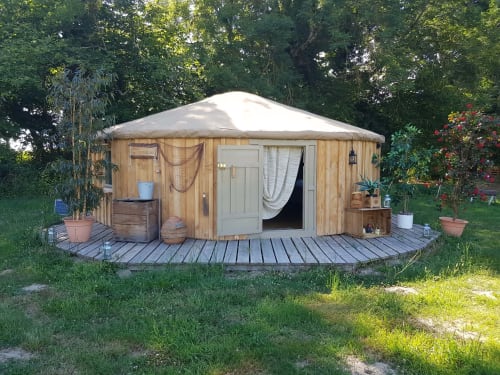 Yourte en bois avec toit conique blanc et terrasse en bois entourée d'un jardin verdoyant à La Toile Sous Les Étoiles à Charron, France