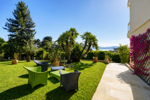 Luxury garden terrace in Cannes with palm trees, manicured lawn, modern seating, magenta bougainvillea, and sea views