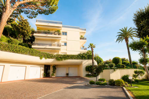 Modern cream-colored villa in Cannes with Mediterranean garden, palm trees, and private driveway