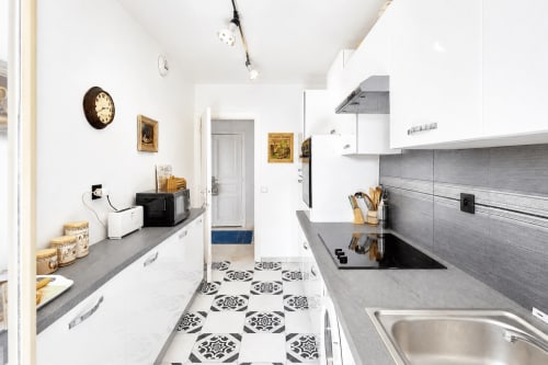 Modern kitchen in Cannes apartment with white cabinets, gray countertops, and patterned black-and-white floor tiles