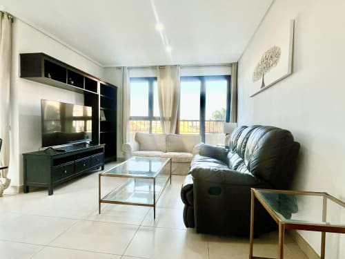 Sala de estar moderna en Pataconablue Rentals en Valencia con balcón con vista al mar, TV, sillón negro y sofá beige