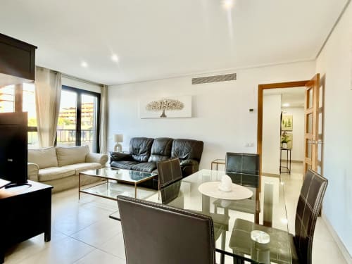 Sala de estar moderna del apartamento de playa en Valencia con sofá de cuero, mesa de comedor y vista al balcón en Pataconablue Rentals