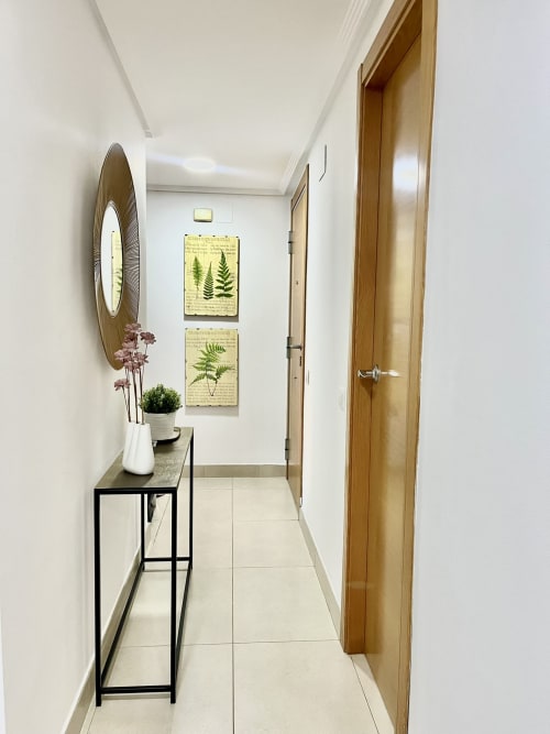 Pasillo moderno en apartamento de playa en Valencia con puertas de madera, espejo, cuadro de helecho y consola con flores