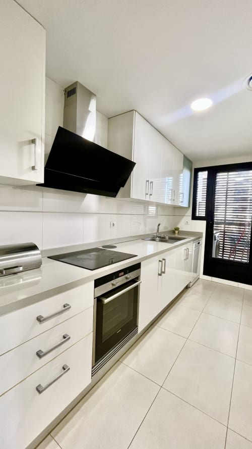 Cocina blanca moderna con campana extractora negra, electrodomésticos de acero inoxidable y pisos de azulejo en apartamento de playa en Valencia