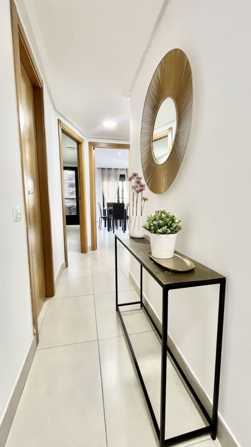 Pasillo de apartamento moderno en Pataconablue Rentals Valencia con puertas de madera, espejo decorativo, plantas en maceta y negro