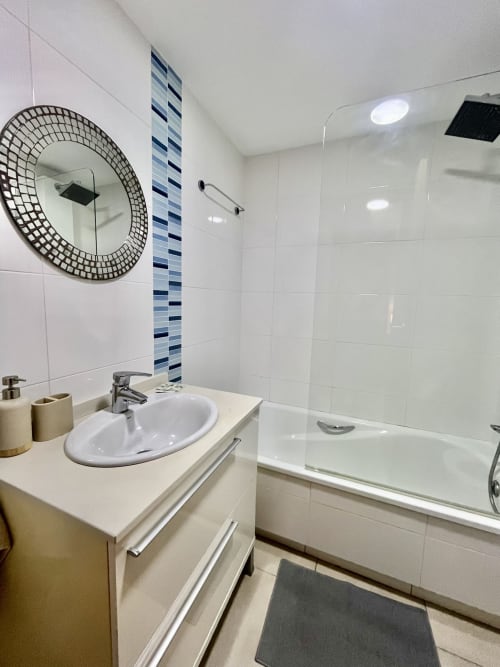 Baño moderno en apartamento de playa en Valencia con lavamanos blanco, espejo redondo, azulejo azul y ducha de cristal