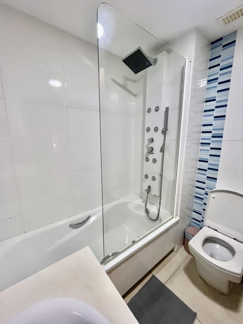Baño moderno con ducha de cristal, azulejos blancos, pared acentuada con rayas azules e inodoro en Rentals Pataconablue