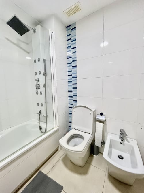 Baño moderno en apartamento de playa en Valencia con ducha, inodoro, bidé, azulejos blancos y franja azul