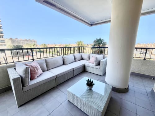 Terraza moderna con sofá gris de mimbre en forma de L, mesa de centro blanca y vistas al mar en el apartamento Pataconablue en Valencia