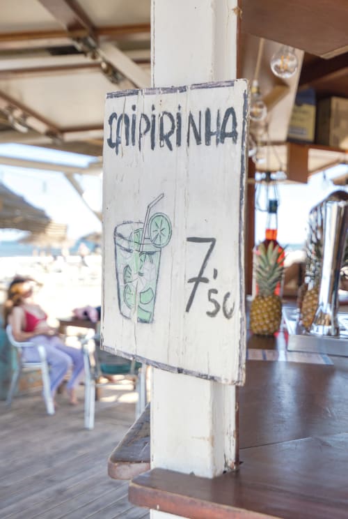 Cartel de cóctel Caipirinha en la playa de Valencia con precio 7,50, zona de bar junto a la piscina visible